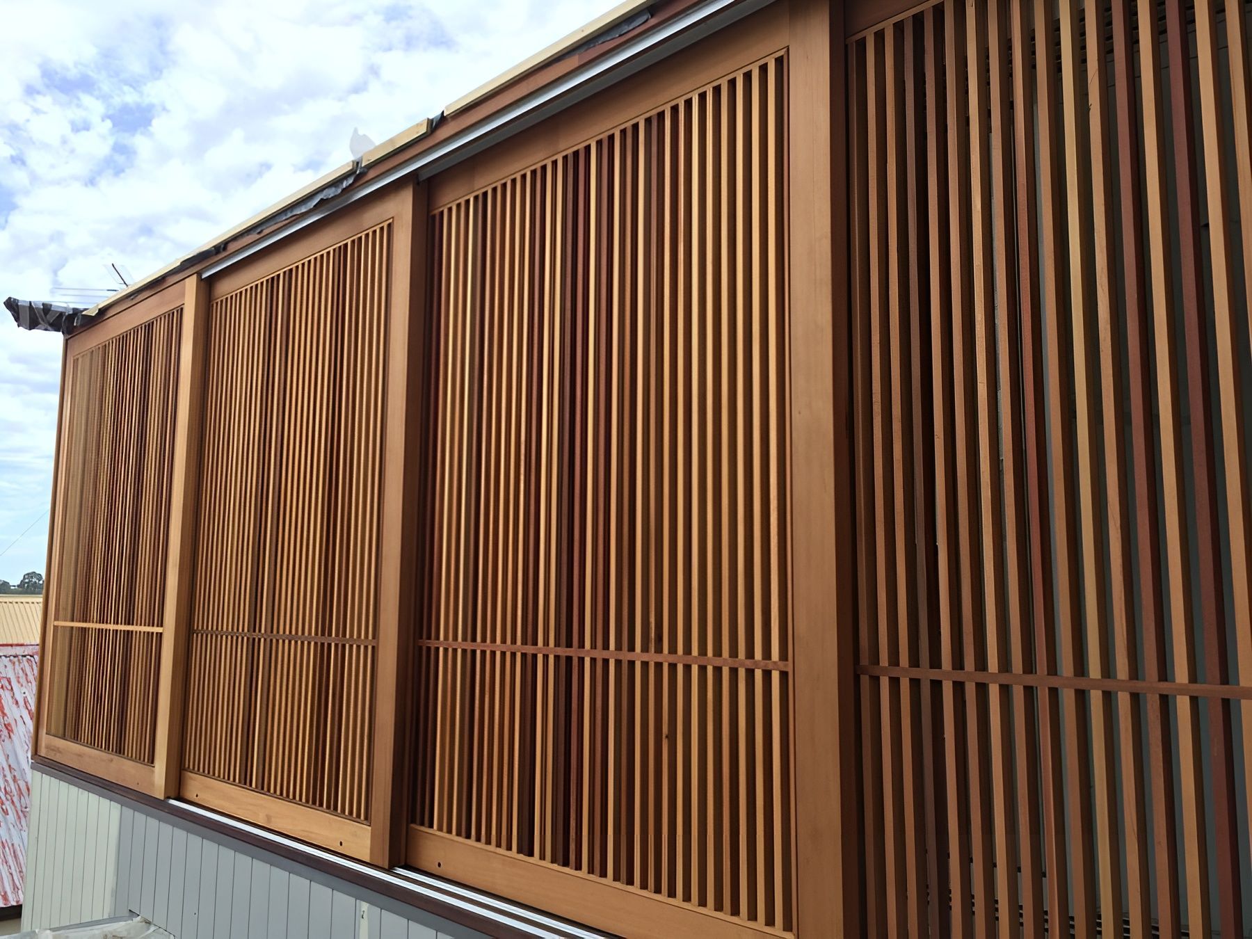 Rust-coloured slatted metal facade on a building, with diagonal sunlight shadows against a blue sky. — Fineworx Joinery in Warnervale, NSW