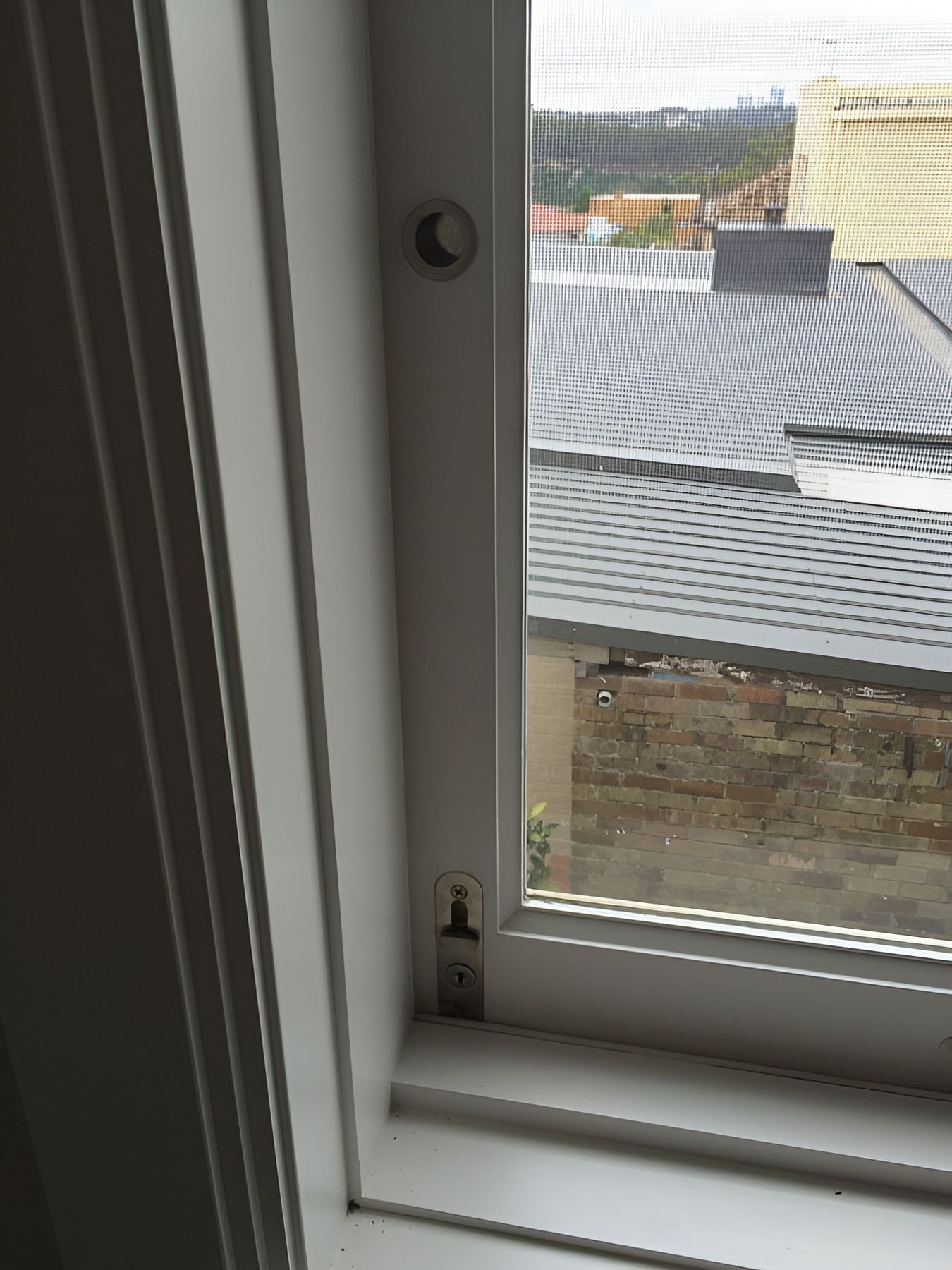 Window with White Frame and Mesh Screen Overlooking Rooftops and A Stone Wall Outside — Fineworx Joinery in Warnervale, NSW