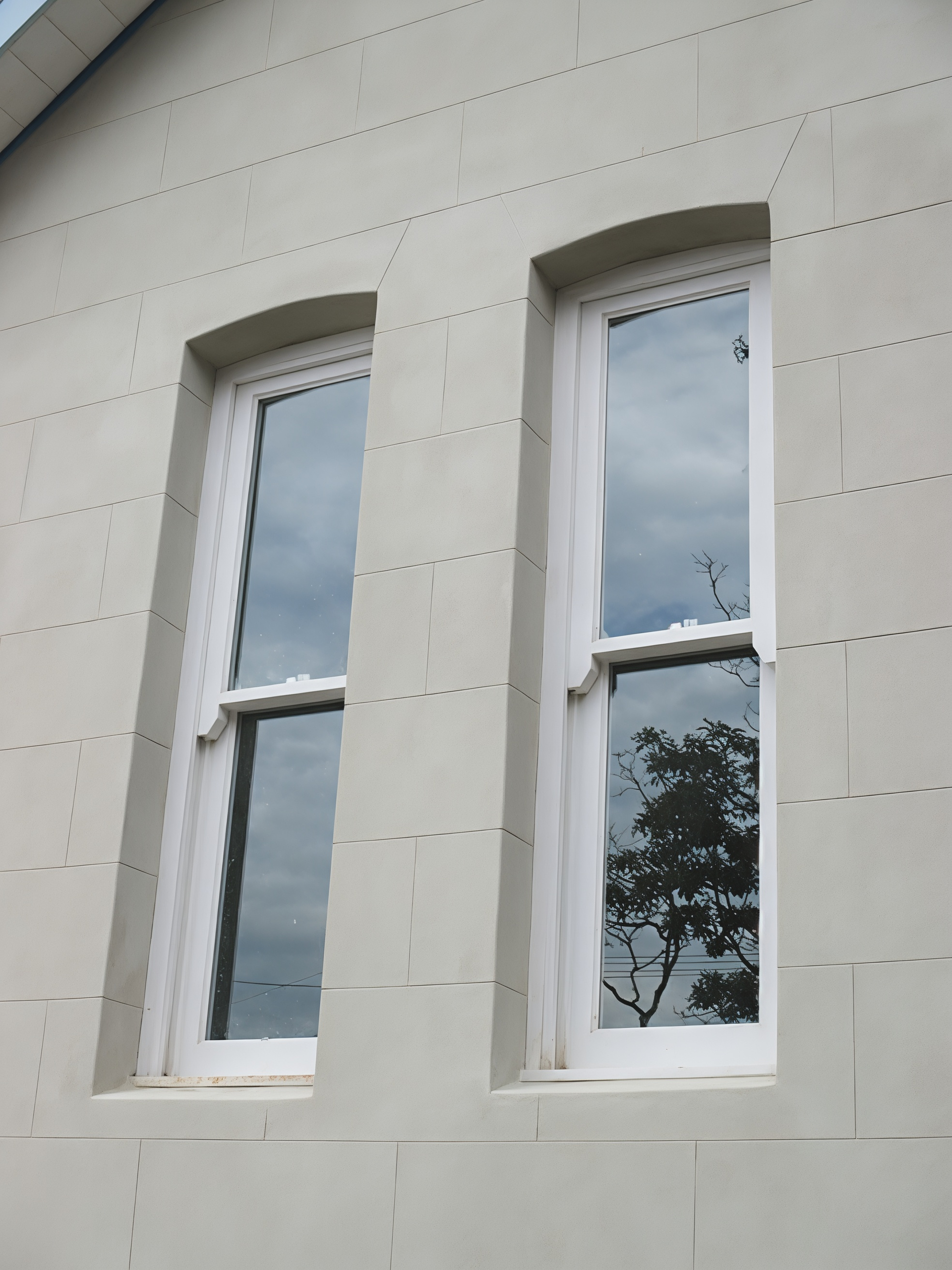 Two White Arched Windows in A Light Stone Wall Reflecting Trees and Cloudy Sky — Fineworx Joinery in Warnervale, NSW