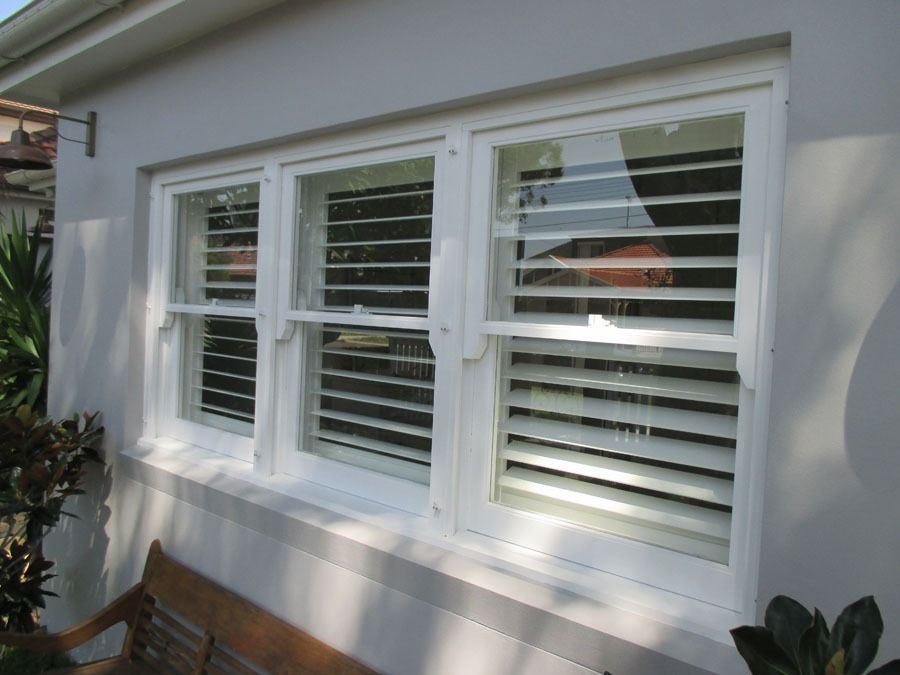 White House Exterior with Three Windows and White Shutters Above a Bench and Plants — Fineworx Joinery in Warnervale, NSW