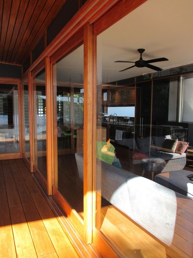 Sunlit Wooden Deck Beside a Glass Walled Living Room with Ceiling Fan and Black Sofa — Fineworx Joinery in Warnervale, NSW