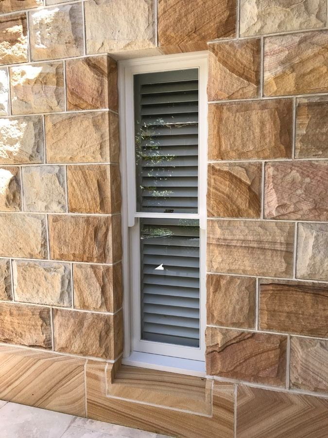 Narrow Window with White Shutters Set in A Tan Stone Exterior Wall — Fineworx Joinery in Warnervale, NSW