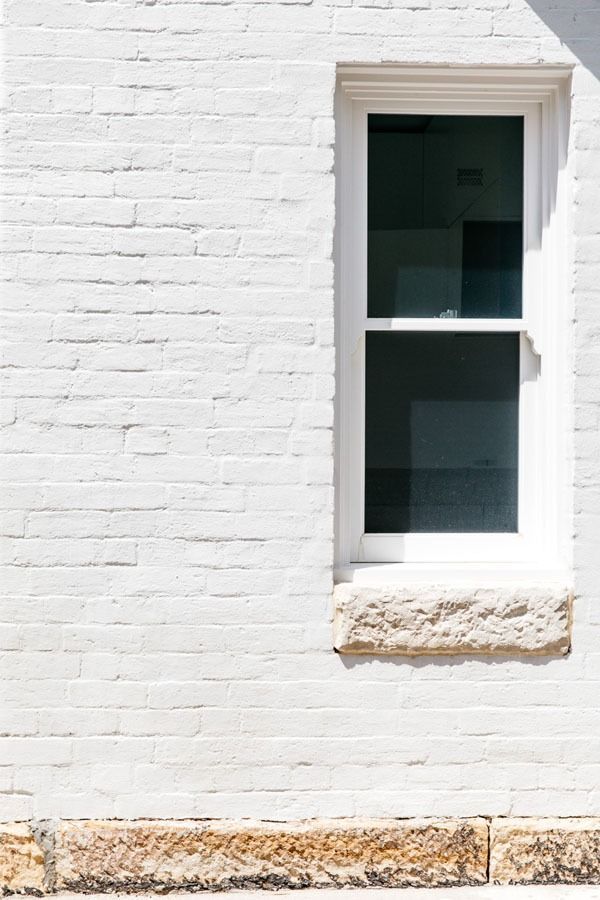 White Brick Wall with A Narrow Window and Weathered Ledge Above a Stone Base — Fineworx Joinery in Warnervale, NSW