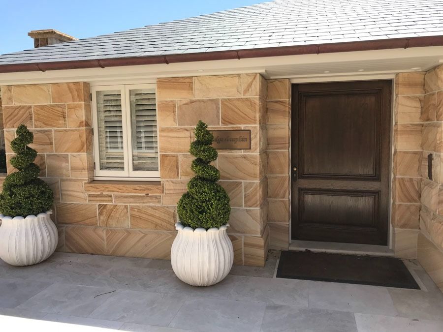 Front Entrance of A Stone House with White Shutters and Dark Wood Door with A Potted Topiary Plant — Fineworx Joinery in Warnervale, NSW