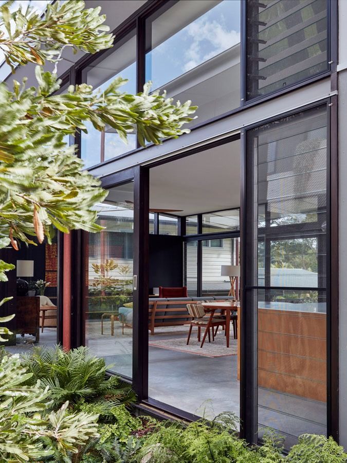 Modern glass home exterior with open sliding doors to a dining area and garden greenery — Fineworx Joinery in Warnervale, NSW