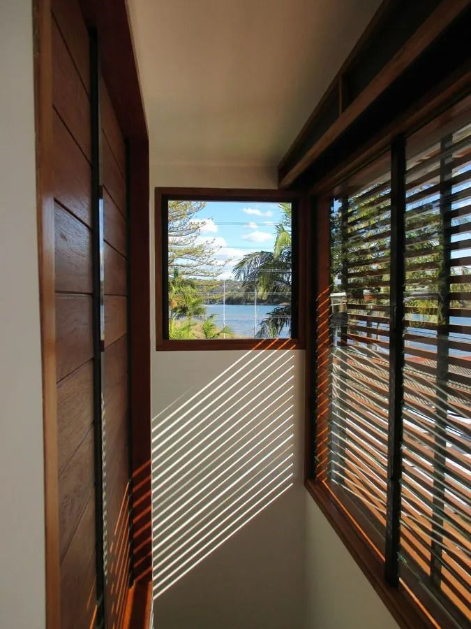 Narrow wooden hallway with slatted blinds, sunlight stripes, and a view of trees and water through the window — Fineworx Joinery in Warnervale, NSW