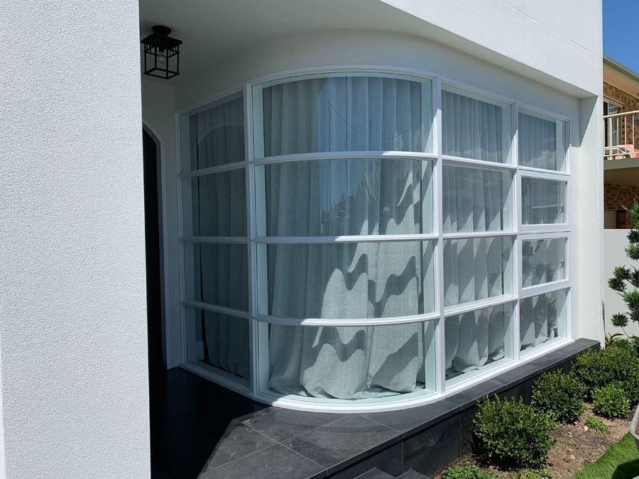 Curved White House Window with Sheer Curtains and A Small Landscaped Garden — Fineworx Joinery in Warnervale, NSW