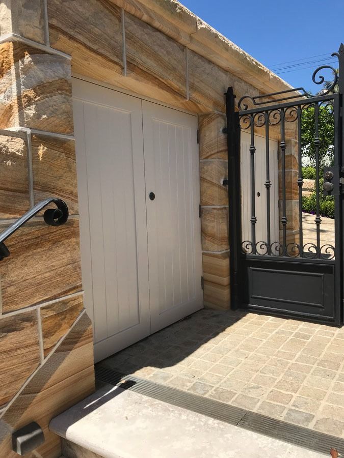 White Double Garage Door Beside Black Wrought Iron Gate — Fineworx Joinery in Warnervale, NSW