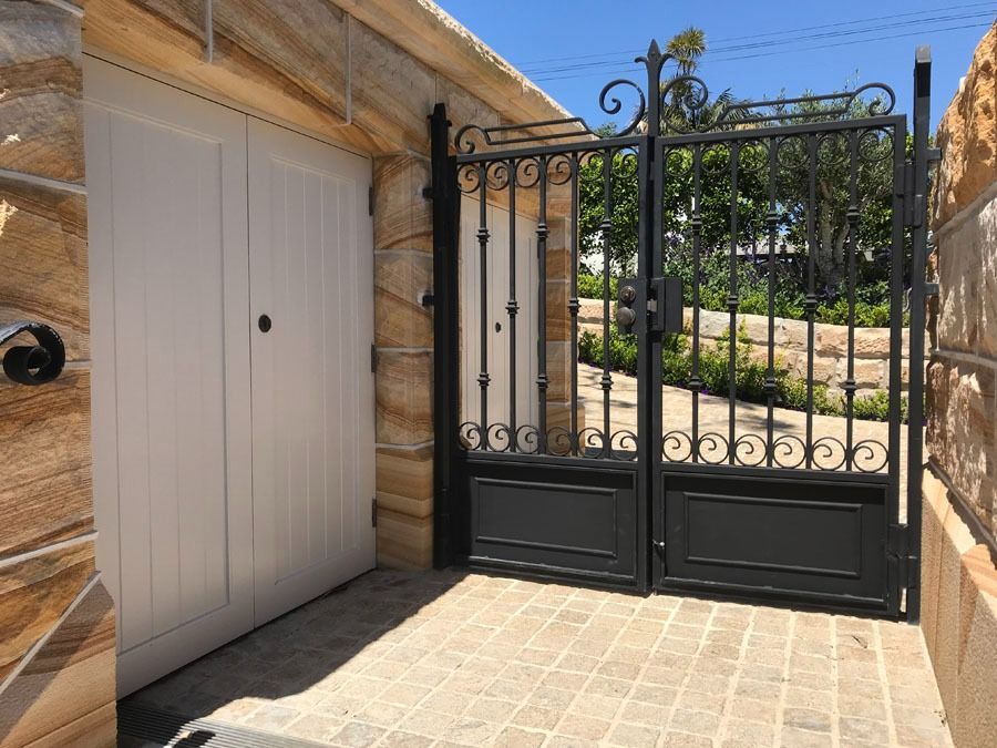 Wrought Iron Gate and White Garage Door at A Stone Lined Courtyard Entrance — Fineworx Joinery in Warnervale, NSW