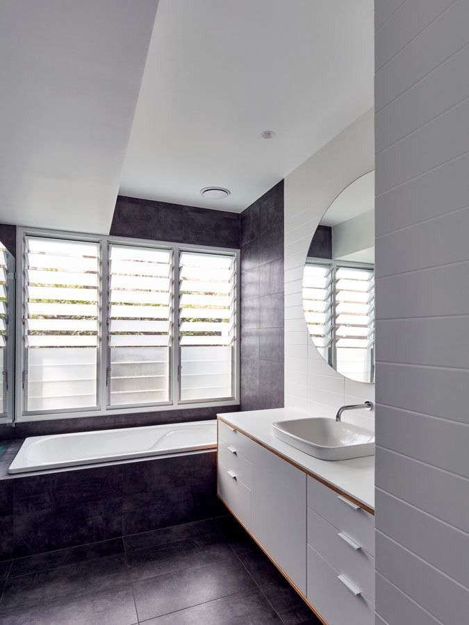 Modern bathroom with white vanity, large mirror, bathtub, and slatted windows letting in light — Fineworx Joinery in Warnervale, NSW