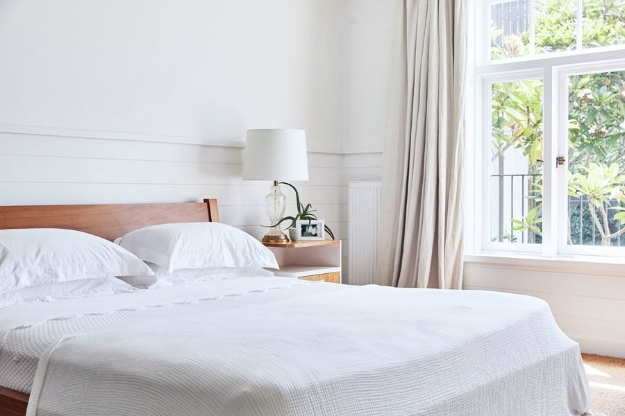 Bright Bedroom with A White Bed and Sunlit Window with Curtains — Fineworx Joinery in Warnervale, NSW