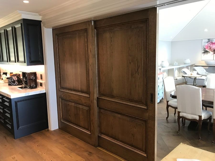 Wood Paneled Sliding Doors Open to A Bright Dining Room Beside a Dark Kitchen — Fineworx Joinery in Warnervale, NSW