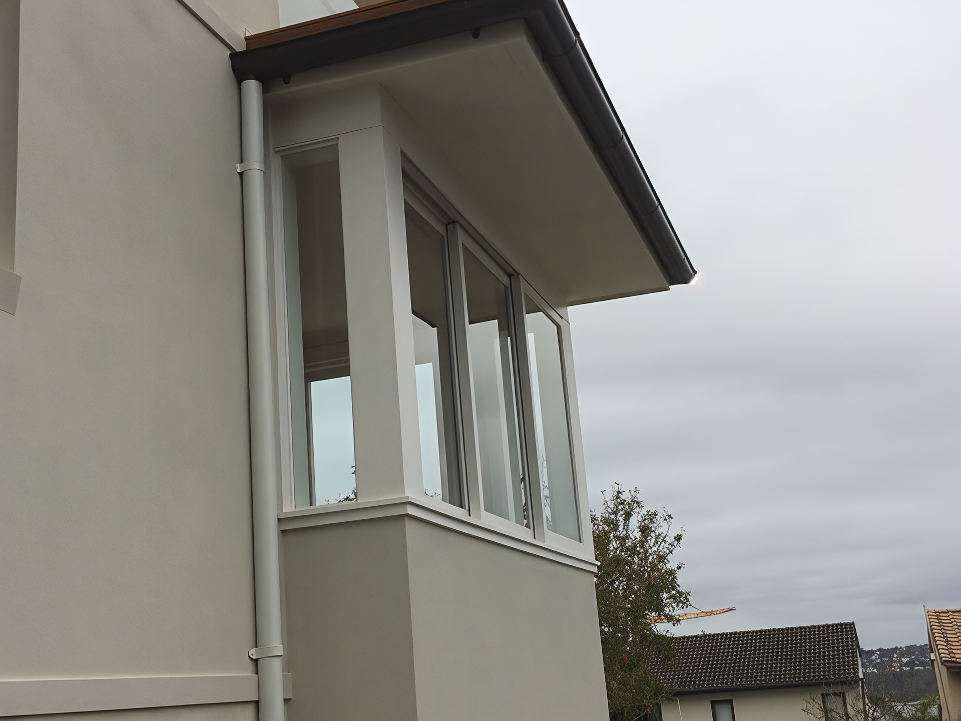 Corner of a grey house with white-framed windows under an overcast sky — Fineworx Joinery in Warnervale, NSW