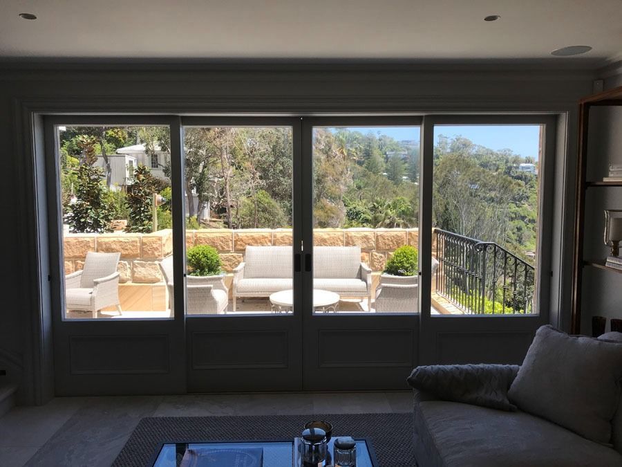 Living Room View Through Large Windows to A Sunny Patio with White Chairs and Stone Wall — Fineworx Joinery in Warnervale, NSW
