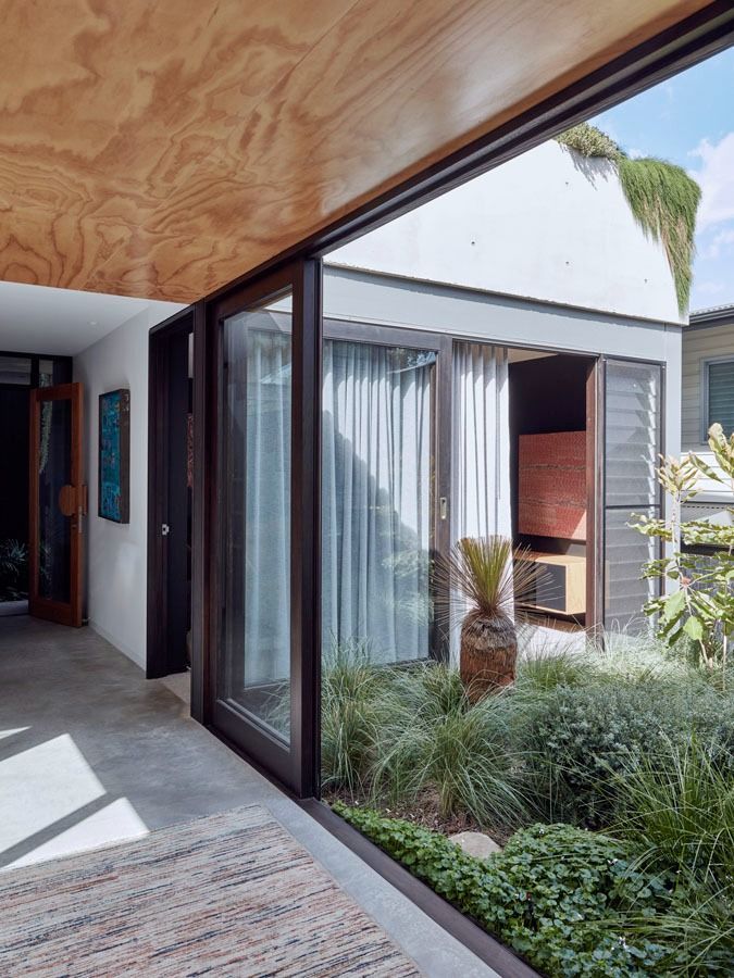 Modern house courtyard with glass sliding doors, wood ceiling, and lush green landscaping — Fineworx Joinery in Warnervale, NSW