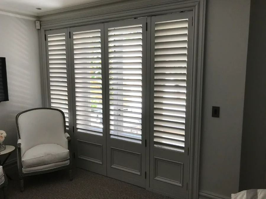 White Shuttered French Doors Beside a Cushioned Chair in A Softly Lit Room — Fineworx Joinery in Warnervale, NSW