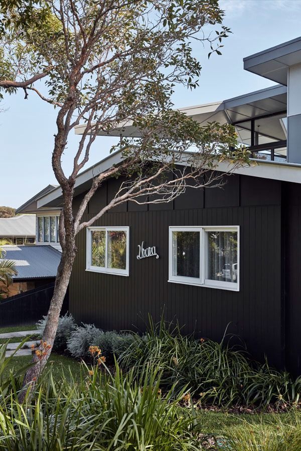 Dark house exterior with white-trimmed windows, tree, and landscaped garden in front — Fineworx Joinery in Warnervale, NSW