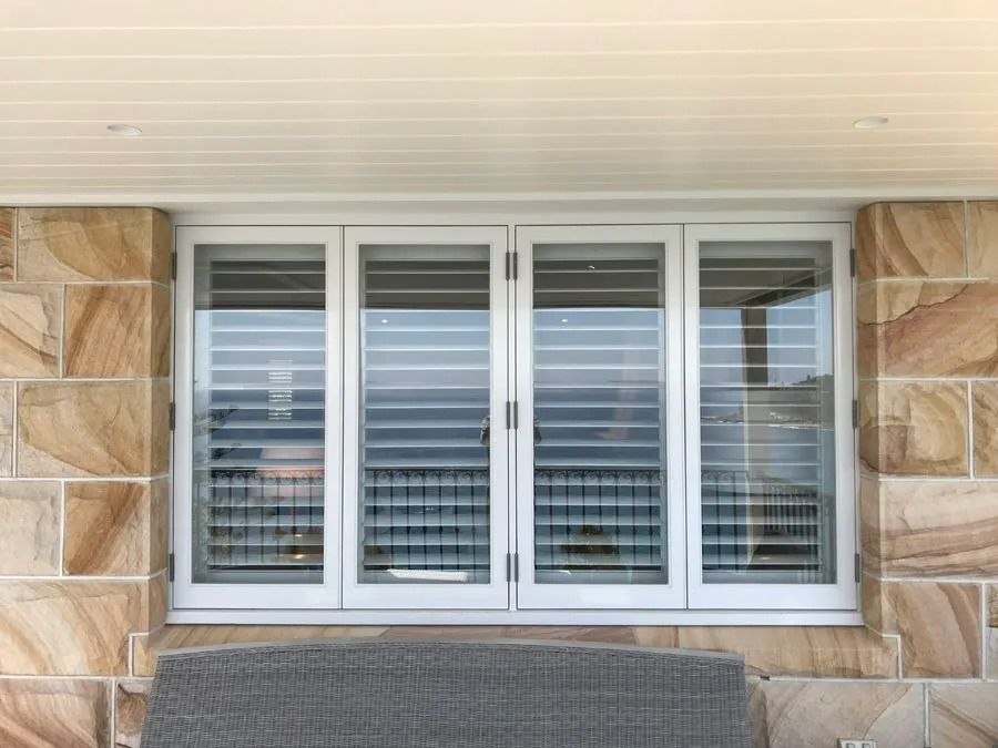 White Window with Closed Blinds and Stone Siding Above a Porch Seat — Fineworx Joinery in Warnervale, NSW