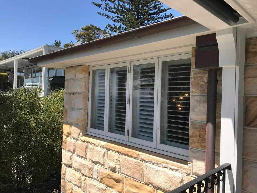 Stone House Exterior with White Shutters and A Black Railing Beside a Patio Roof — Fineworx Joinery in Warnervale, NSW