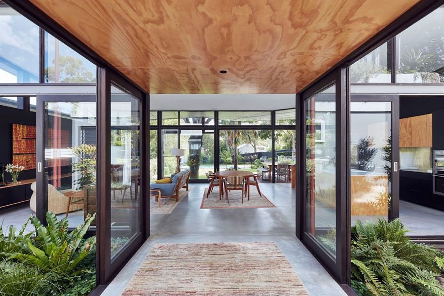 Modern Glass Hallway Opening to A Sunlit Patio with Seating and Lush Plants — Fineworx Joinery in Warnervale, NSW