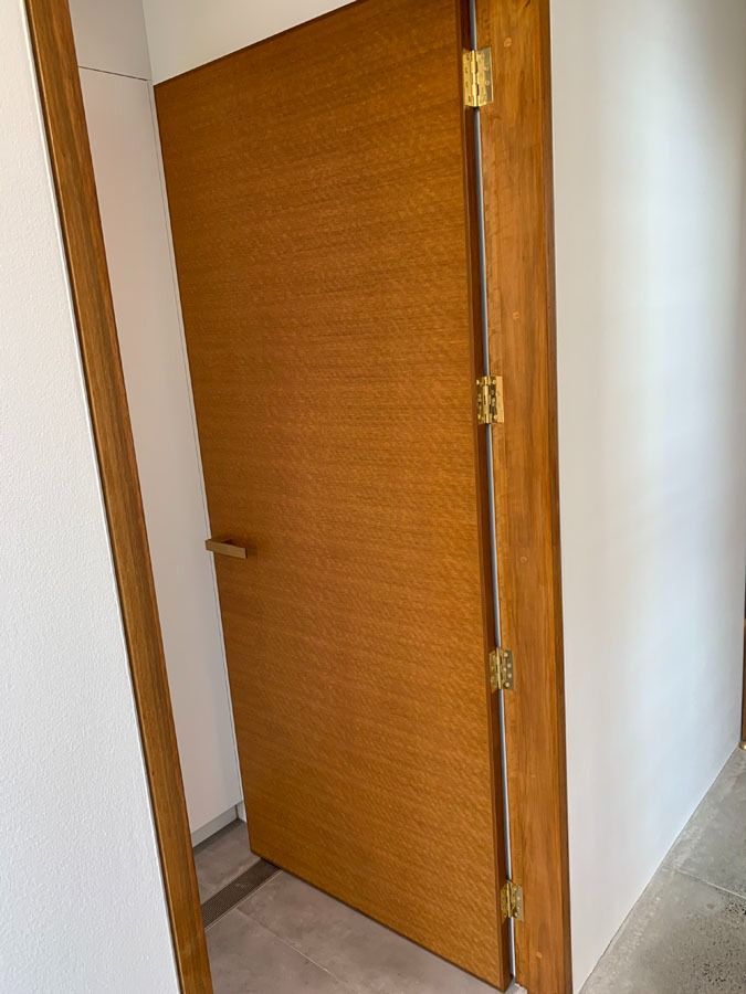 Partially Open Wooden Door with Brass Hinges in A White Hallway — Fineworx Joinery in Warnervale, NSW