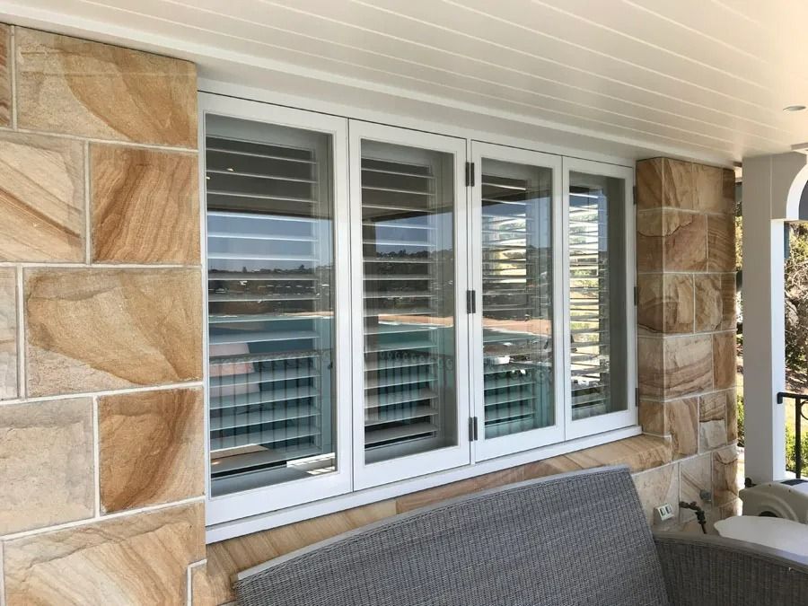 White Shuttered Window on A Beige Stone Porch with A Cushioned Bench in Front — Fineworx Joinery in Warnervale, NSW