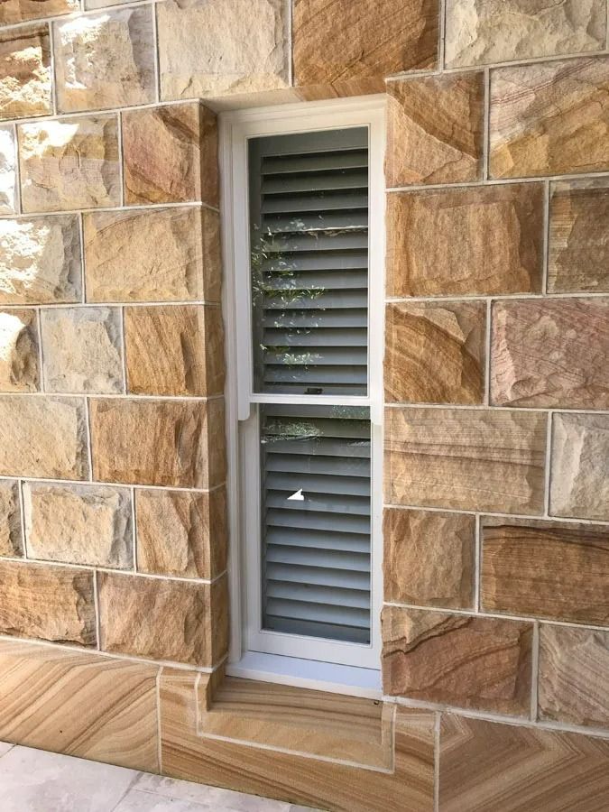 Narrow White Louvered Window Set in Tan Stone Wall with Beige Trim and Sill — Fineworx Joinery in Warnervale, NSW