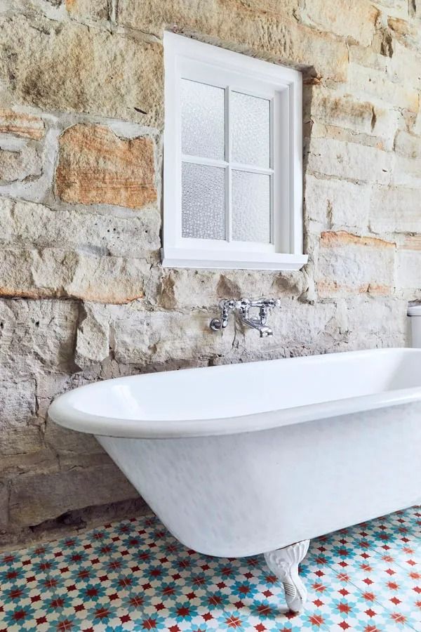 White Clawfoot Bathtub Beside a Stone Wall and Small Window in A Patterned Tile Bathroom — Fineworx Joinery in Warnervale, NSW