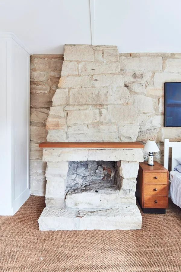 Stone Fireplace with Wooden Mantel in A Light Colored Bedroom with A Wicker Rug and Bedside Table — Fineworx Joinery in Warnervale, NSW