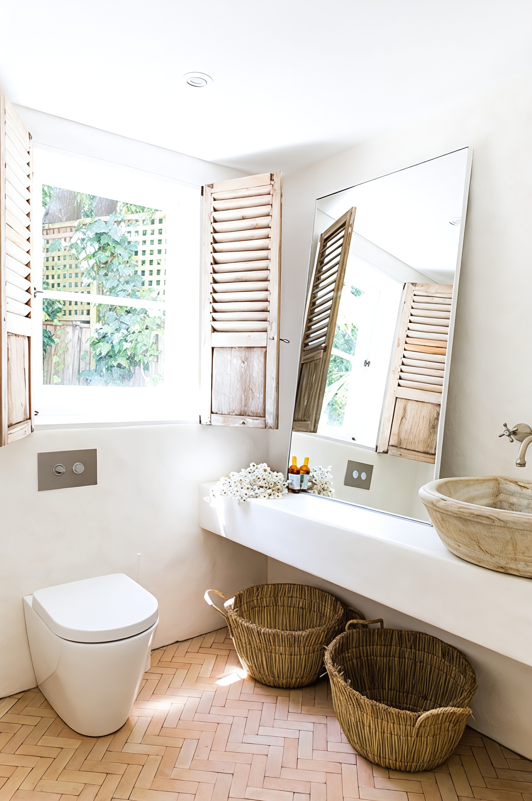 Bright bathroom with white walls, large mirror, wicker baskets, and a toilet by a window. — Fineworx Joinery in Warnervale, NSW
