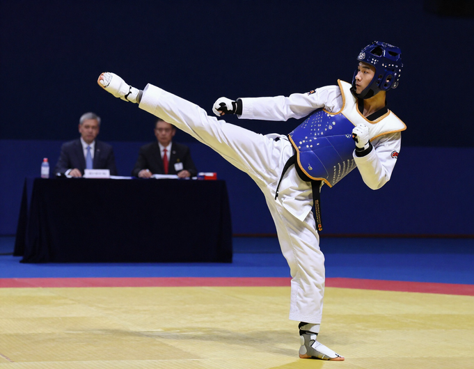 Taekwondo athlete in sparring gear kicking on a tournament mat