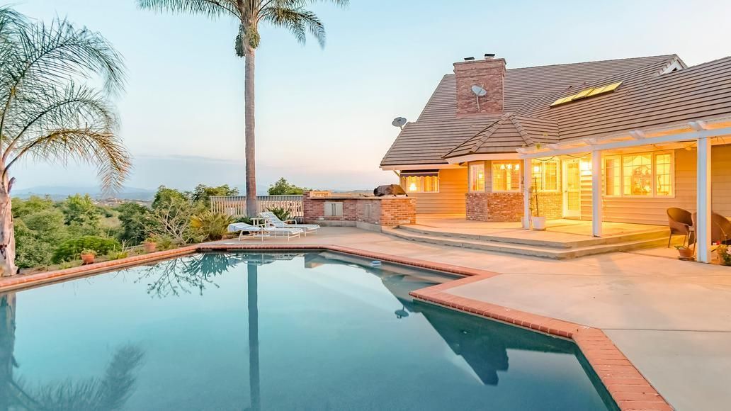The back yard of a home on a hill. There's a pool in the foreground.