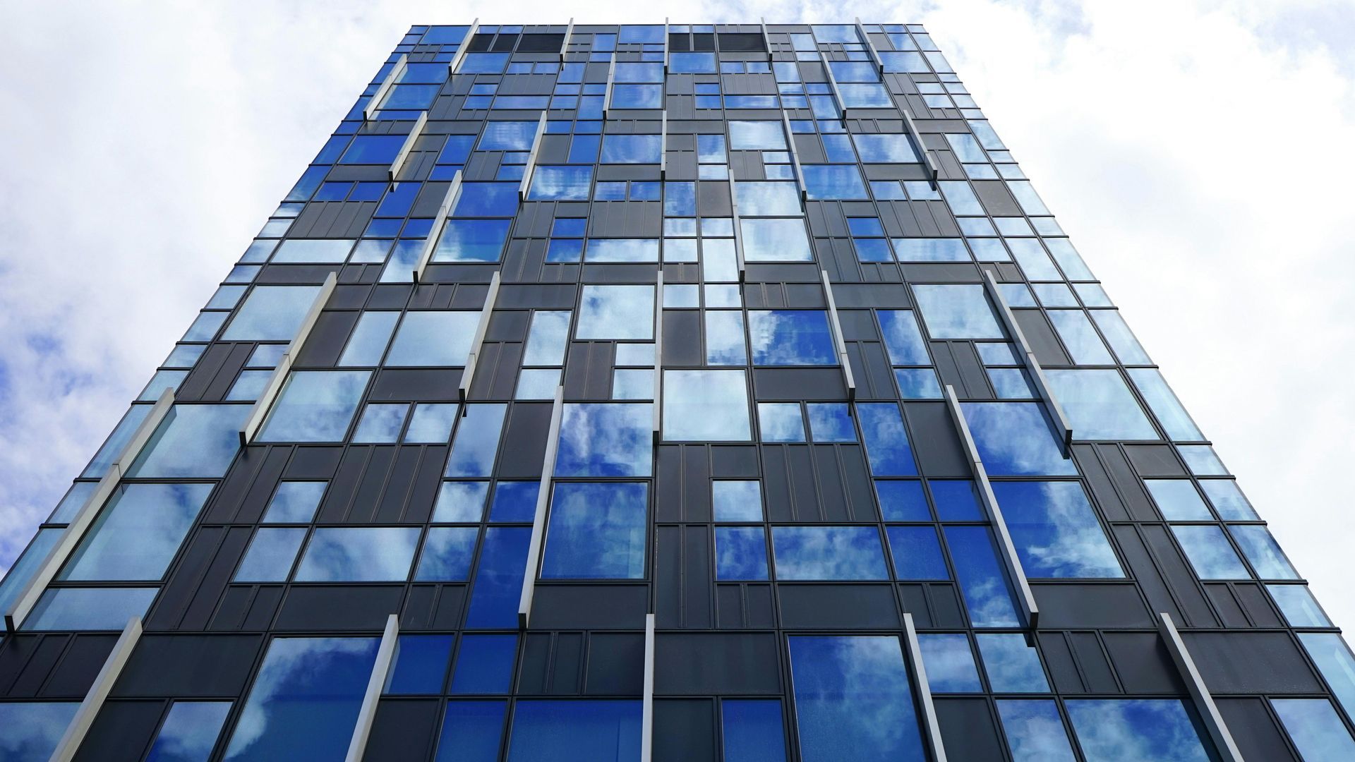 Two people shaking hands in front of a window in a high rise building.