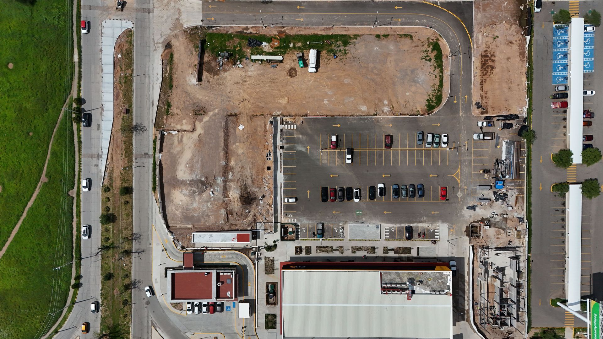 Aerial view of a parking lot beside a large building, with scattered cars and dirt construction area.