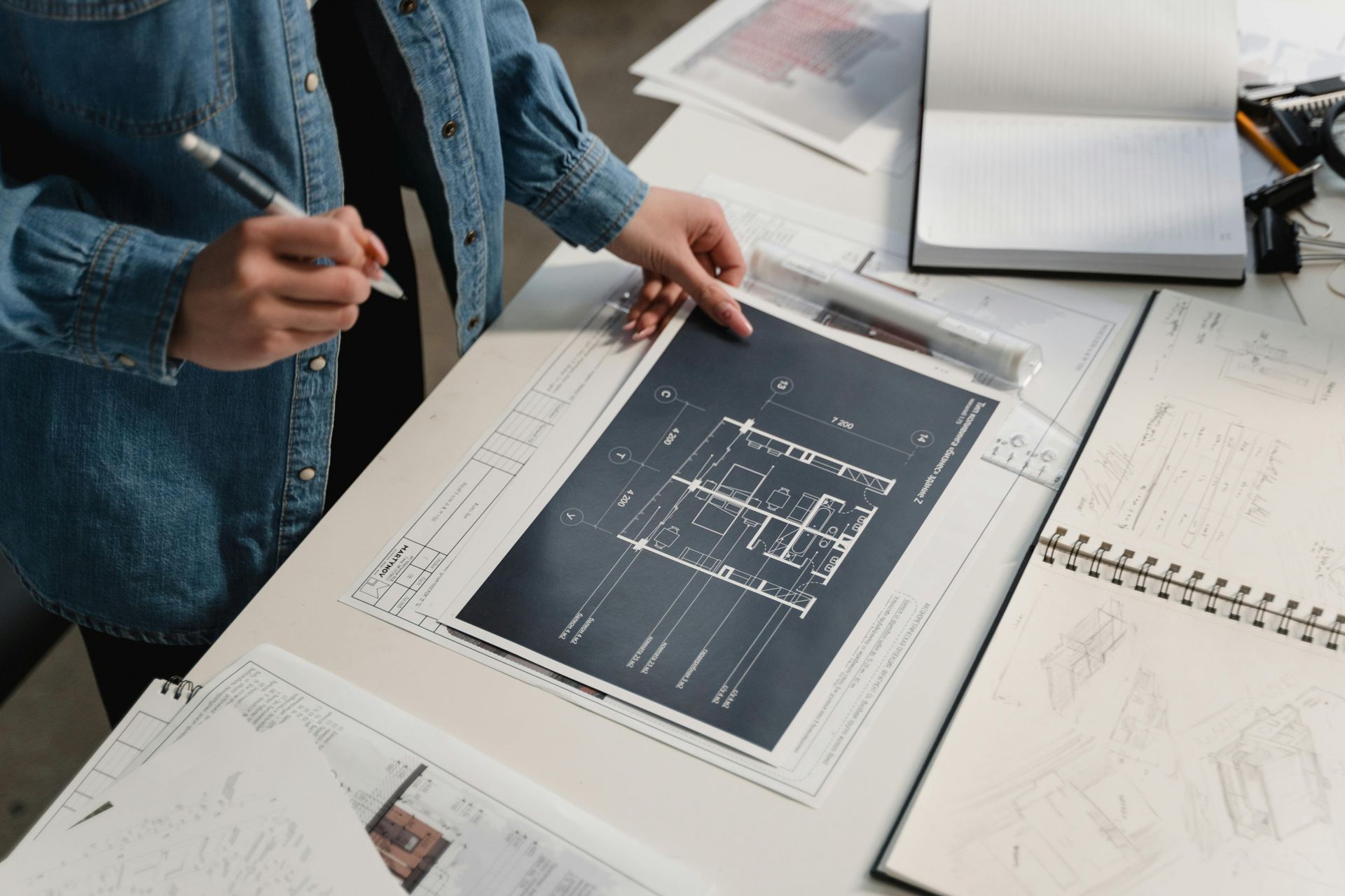 A person draws a line in pencil with a straight edge on blueprints.