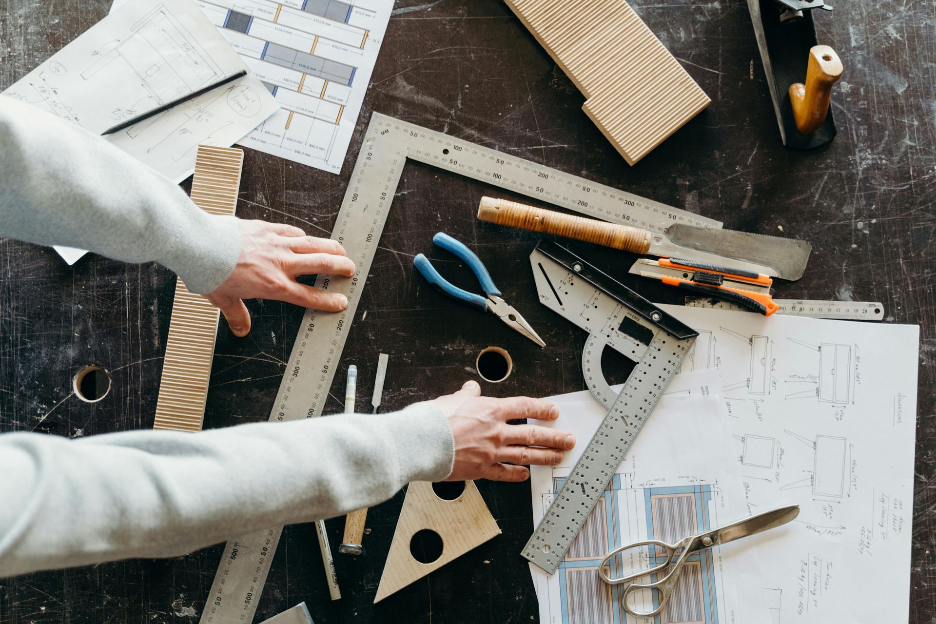 Blueprints and design tools on a table. Someone is doing work with them.