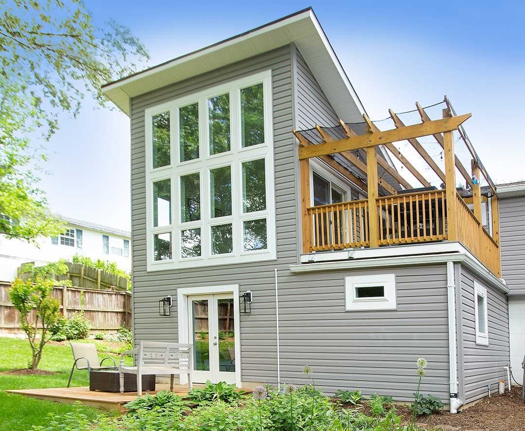Modern gray house with large windows and a wooden deck under construction in a green yard