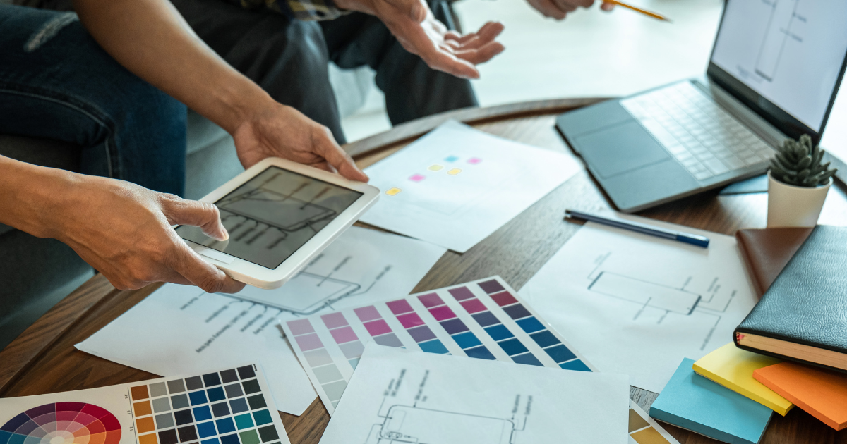 People work around a messy desk, looking at a tablet.