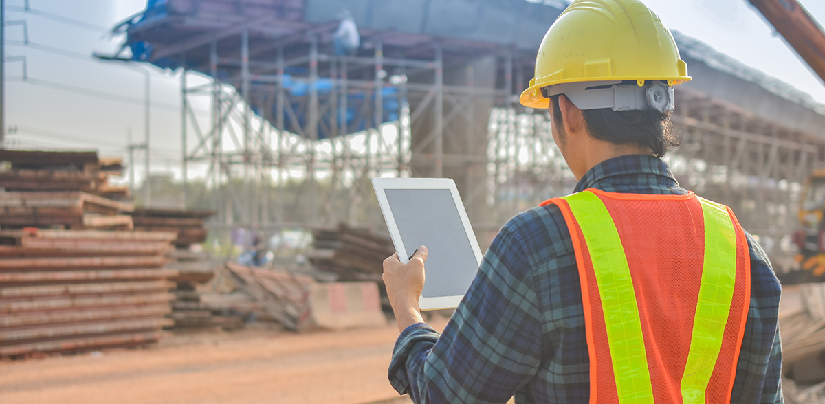 A construction worker looks at a tablet on a construction site.