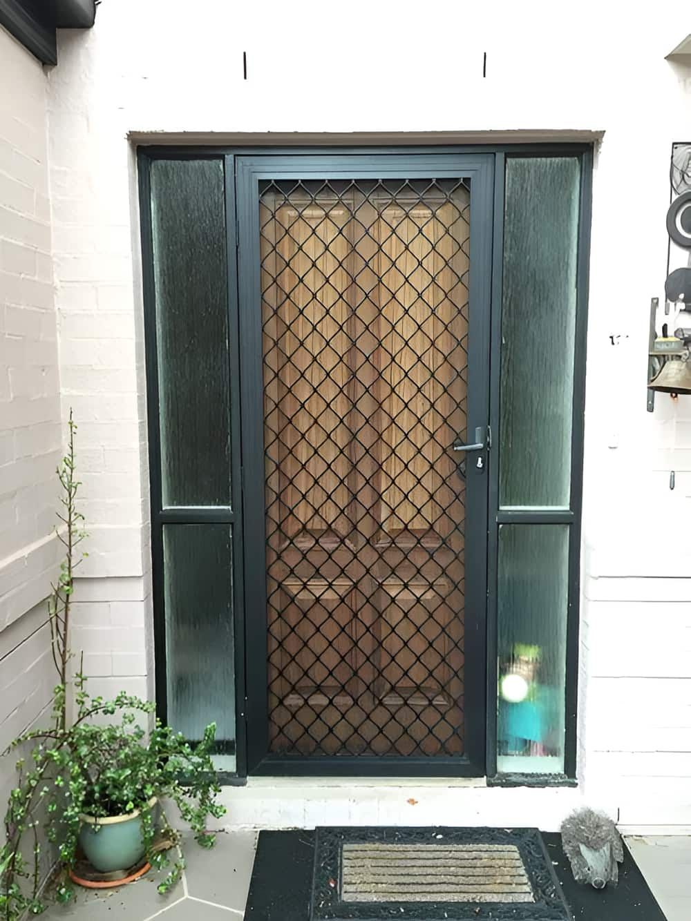 A Black Door With A Diamond Pattern On It Is Sitting On A Porch Next To A Potted Plant — Screen Factory In Ocean Shores, NSW
