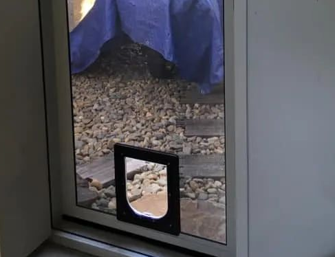 Small pet door in a glass door opening to a rocky outdoor area — Screen Factory In Ocean Shores, NSW