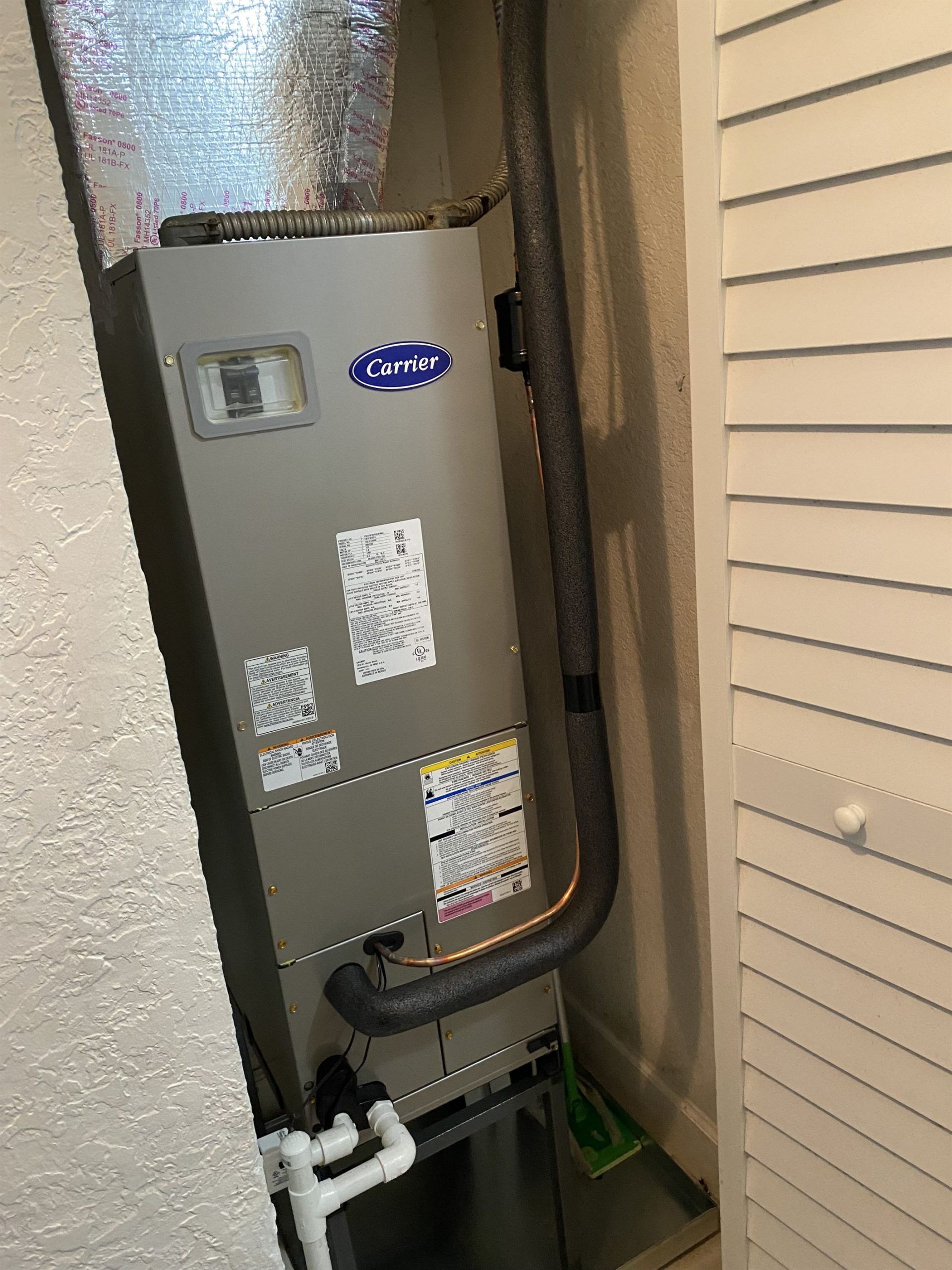 An American Standard HVAC unit in a utility closet with vent pipes and drainage.
