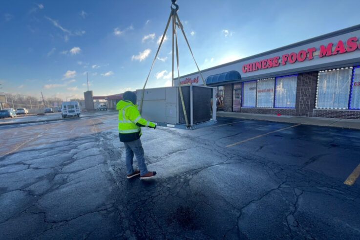 Man in yellow vest guides a concrete structure being lifted by a crane near a Chinese Foot Massage storefront.