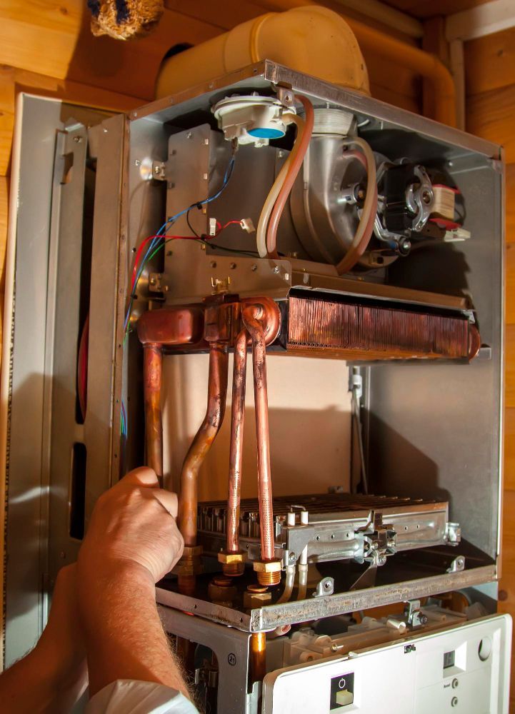 Person working on an open gas boiler, copper pipes visible.