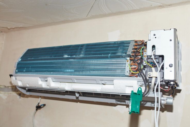 Wall-mounted air conditioner unit, partially disassembled, showing internal coils and wiring.