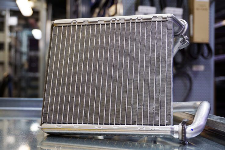 Car heater core with metal fins and tubes, on a reflective surface.