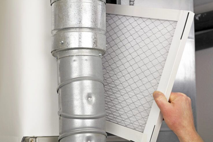 Hand replacing a white air filter near silver ductwork.