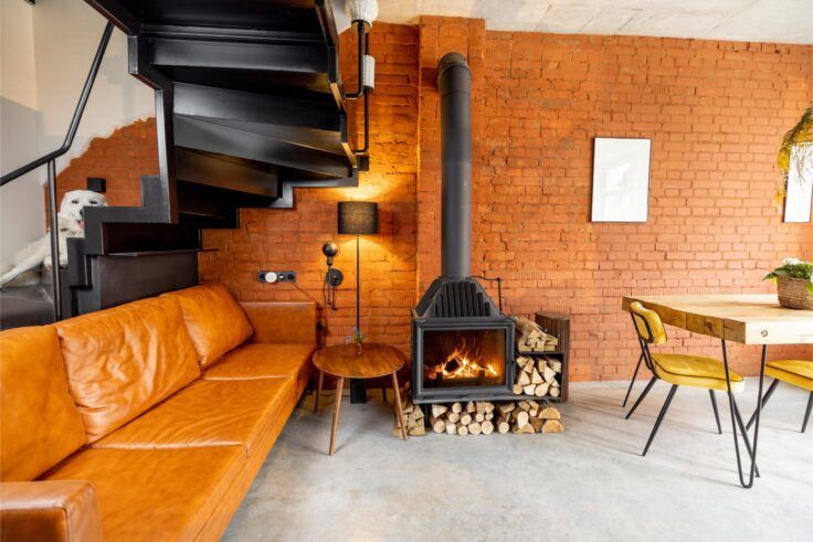Living room with orange brick wall, leather sofa, fireplace, and spiral staircase.