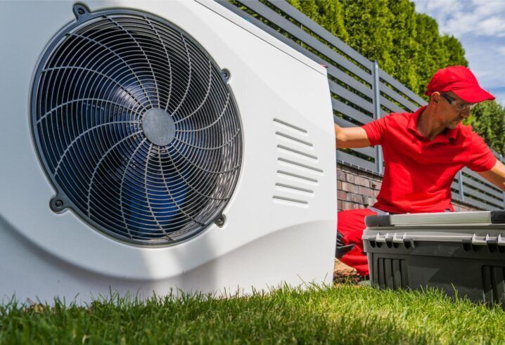 HVAC technician working on an outdoor unit next to a fence in a grassy yard.