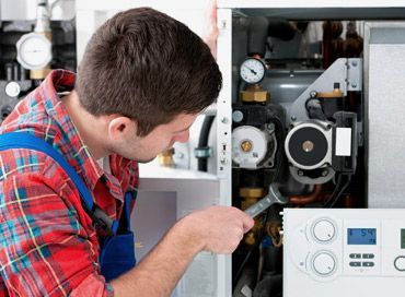 Man in work clothes uses a wrench on a heating system.